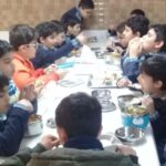 دانش‌آموزان در حال خوردن غذا و صرف وعده‌ی مشترک در سالن غذاخوری مدرسه