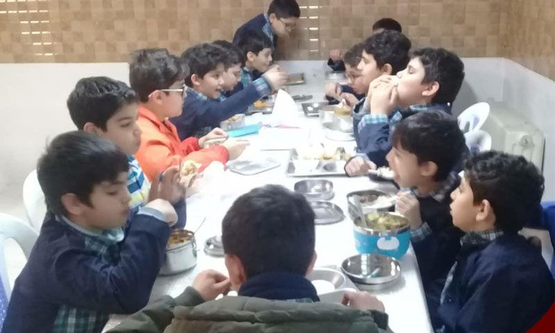 دانش‌آموزان در حال خوردن غذا و صرف وعده‌ی مشترک در سالن غذاخوری مدرسه