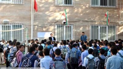 دسته‌جمعی دانش‌آموزان مدرسه در حیاط به هنگام برگزاری مراسم با پرچم‌های رنگین