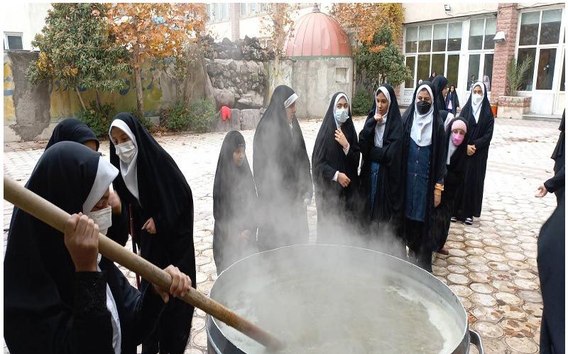 دانش‌آموزان دختر با لباس مدرسه‌ای در حیاط مدرسه دور یک دیگ بزرگ ایستاده‌اند و در یک آزمایش علمی/فعالیت STEM شرکت می‌کنند