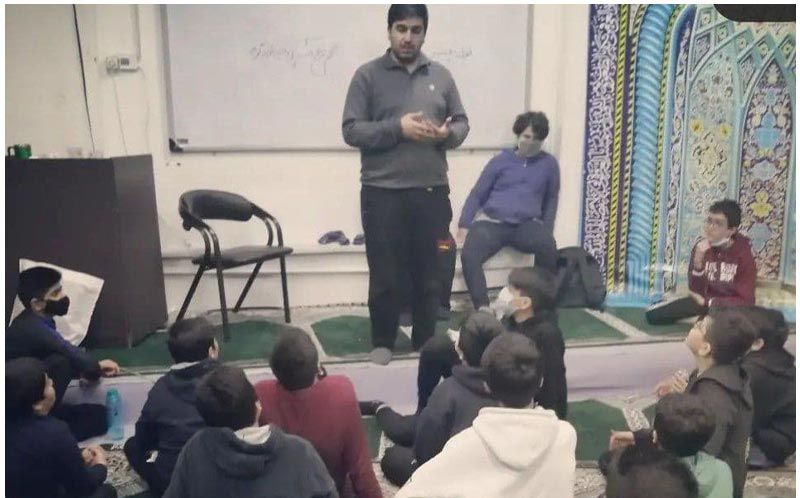 دانش‌آموزان در حال شرکت در جلسه‌ای تعاملی و گروهی با فرهبری که در وسط ایستاده و با دانش‌آموزان صحبت می‌کند