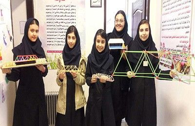 دانش‌آموزان دختر در حال نمایش یک ساختار هندسی با اشکال زرد و سیاه در کلاس درس، نشان‌دهنده فعالیت تعاملی STEM و یادگیری تجربی در محیط آموزشی