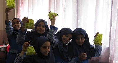 گروهی از دانش‌آموزان دختر در لباس یونیفرم مدرسه کتاب‌های سبز رنگ در دست دارند و برای عکس جمع شده‌اند