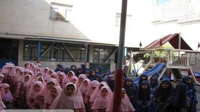 گروهی از دانش‌آموزان دختر با حجاب صورتی و سفید در حیاط مدرسه در حین یک فعالیت یا مراسم جمعی