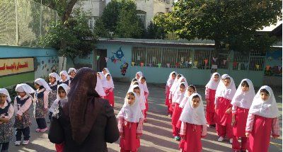 دانش‌آموزان در لباس یکنواخت سفید و قرمز ایستاده در حیاط مدرسه، در حال شرکت در صبح‌انجمن یا تجمع مدرسه