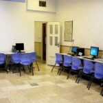 نمایی از سایت کامپیوتری مدرسه با صندلی های آبی رنگ و رایانه های رومیزی