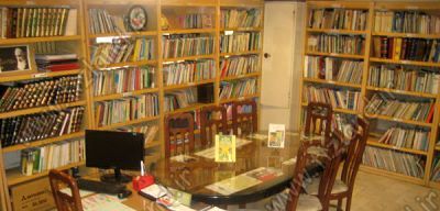 کتابخانه مدرسه با قفسه‌های بلند پُر از کتاب‌ها، میز و صندلی‌های مطالعه، و رایانه